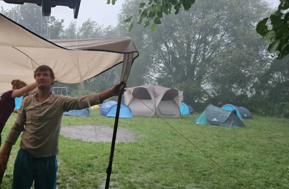 Christian spannt bei starkem Regen ein Tarp über den Zeltplatz